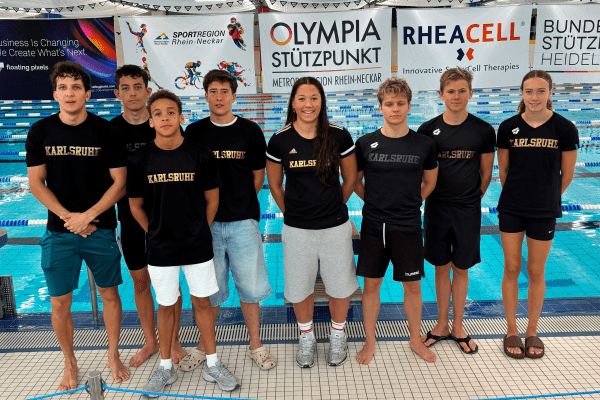 Gruppe von acht Schwimmern in schwarzen Shirts mit der Aufschrift "Karlsruhe" an einem Schwimmbecken.