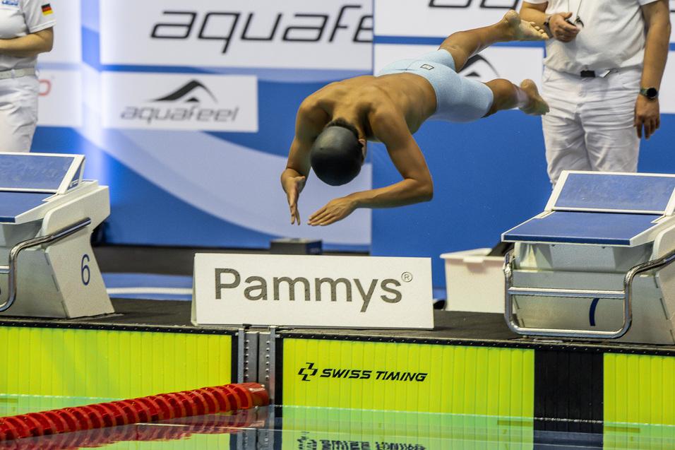Wettkampfschwimmer springt von der Startsprungblöcke in ein Becken während eines Wettbewerbs.