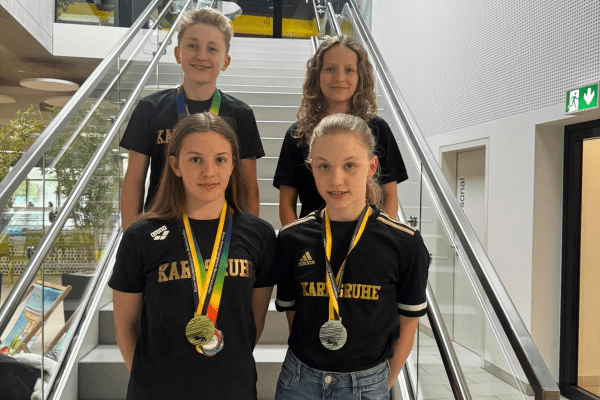 Vier Kinder mit Medaillen stehen auf einer Treppe in Sportkleidung mit Aufdruck „Karlsruhe“.
