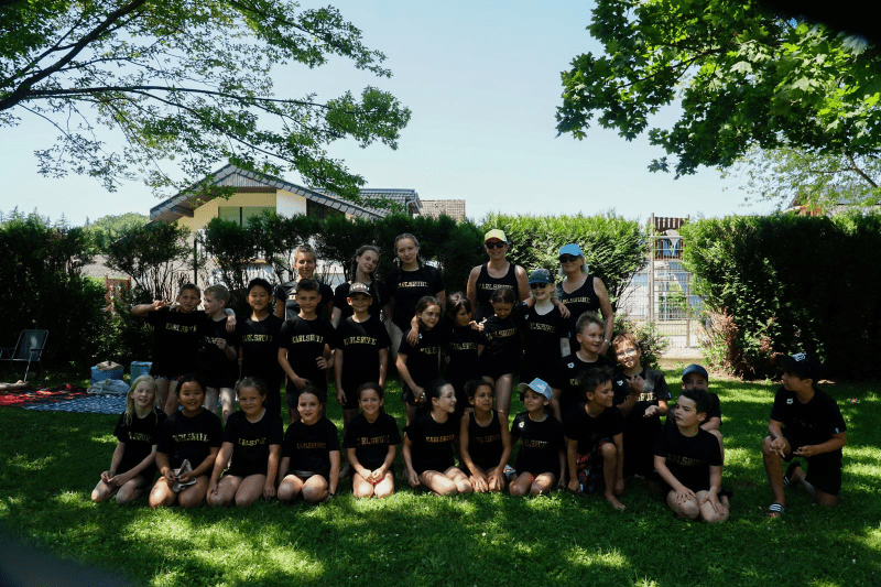 Gruppenshot von Kindern in schwarzen T-Shirts im Freien, umgeben von Bäumen und einem Wohnhaus im Hintergrund.