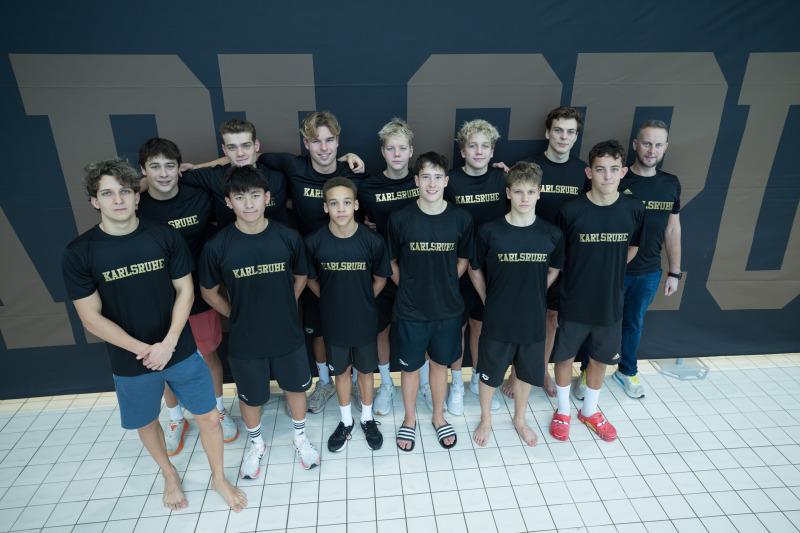 Gruppe von 12 Jugendlichen in T-Shirts mit dem Schriftzug „Karlsruhe“, posierend vor einer dunklen Wand.