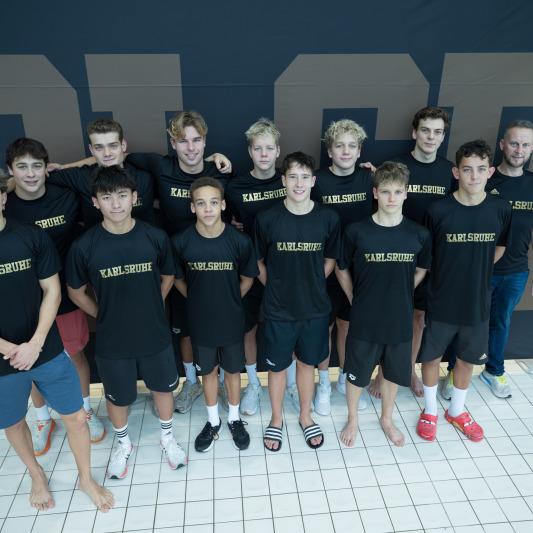 Gruppe von 12 Jugendlichen in T-Shirts mit dem Schriftzug „Karlsruhe“, posierend vor einer dunklen Wand.