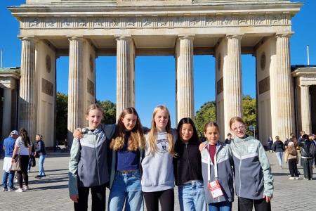 Gruppe von fünf Mädchen posiert am Brandenburger Tor in Berlin an einem sonnigen Tag.