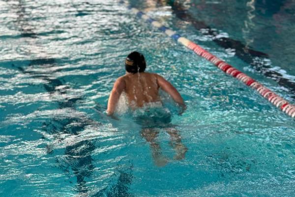 Schwimmerin in einem Becken, die mit sichtbarem Spritzwasser krault. Die Wasseroberfläche ist klar und reflektiert Licht.