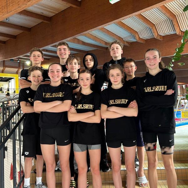 Gruppe von zehn Jugendlichen in schwarzen T-Shirts mit Aufdruck „Karlsruhe“ posiert auf einer Treppe in einem Schwimmbad.