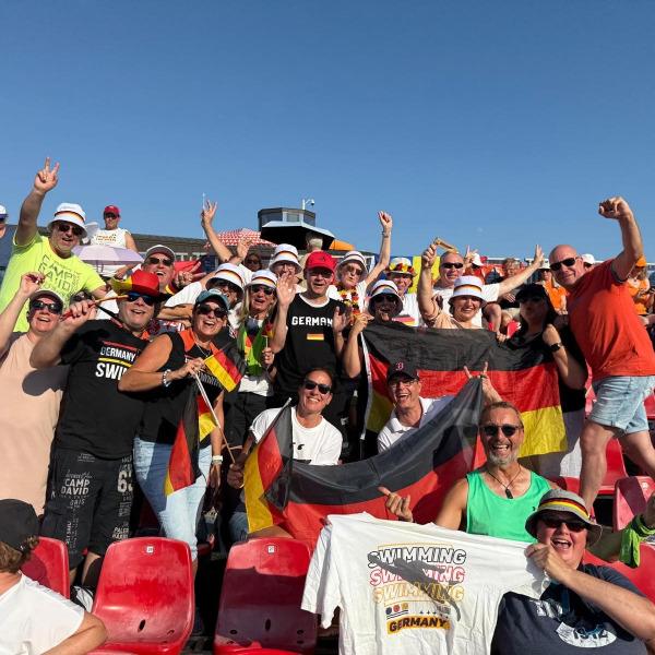 Gruppe von Fans mit deutschen Flaggen und T-Shirts, die in einem Sportstadion jubeln und feiern.