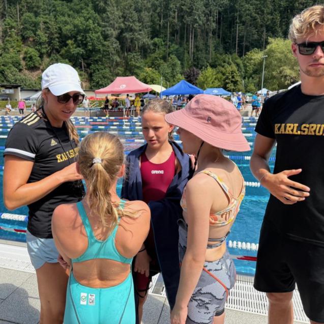 Vier Schwimmerinnen und Schwimmer unterhalten sich am Beckenrand bei einem Wettkampf im Freiwasser.