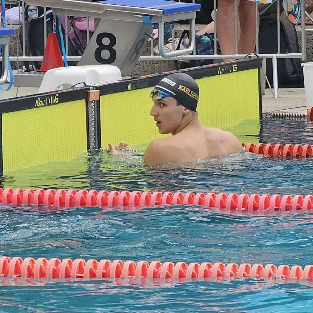 Schwimmer in der Badehose mit Kappe schaut über den Beckenrand, Schwimmhalle mit gepunkteten Schwimmbahnen im Hintergrund.