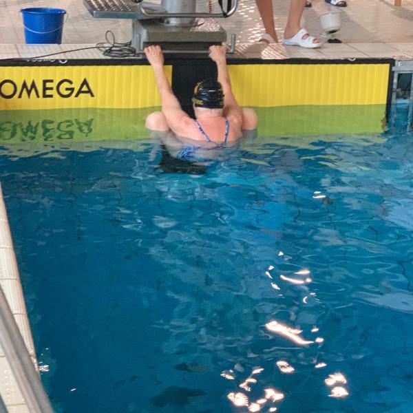 Schwimmerin in einer blauen Badekleidung hängt am Beckenrand eines Schwimmbeckens mit Omega-Startblock.