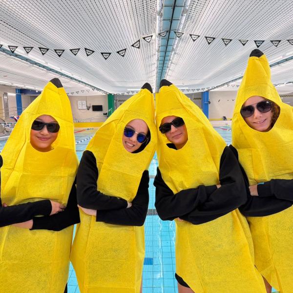 Vier Personen in gelben Bananenkostümen stehen am Rand eines Schwimmbeckens und tragen Sonnenbrillen.