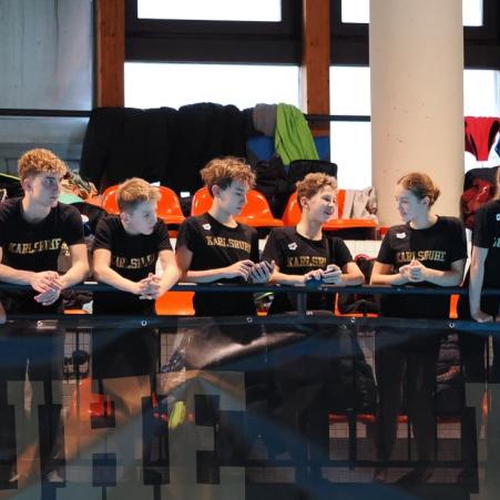 Gruppe junger Sportler in schwarz-gelben T-Shirts lehnt an einer Balustrade in einer Sporthalle.