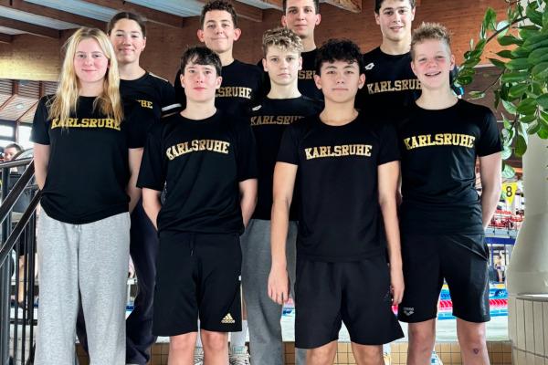 Gruppe von neun Jugendlichen in schwarzen T-Shirts mit "Karlsruhe" auf einer Treppe in einem Sporteinrichtungsbereich.
