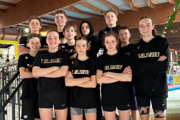 Gruppe von zehn Jugendlichen in schwarzen T-Shirts mit Aufdruck „Karlsruhe“ posiert auf einer Treppe in einem Schwimmbad.