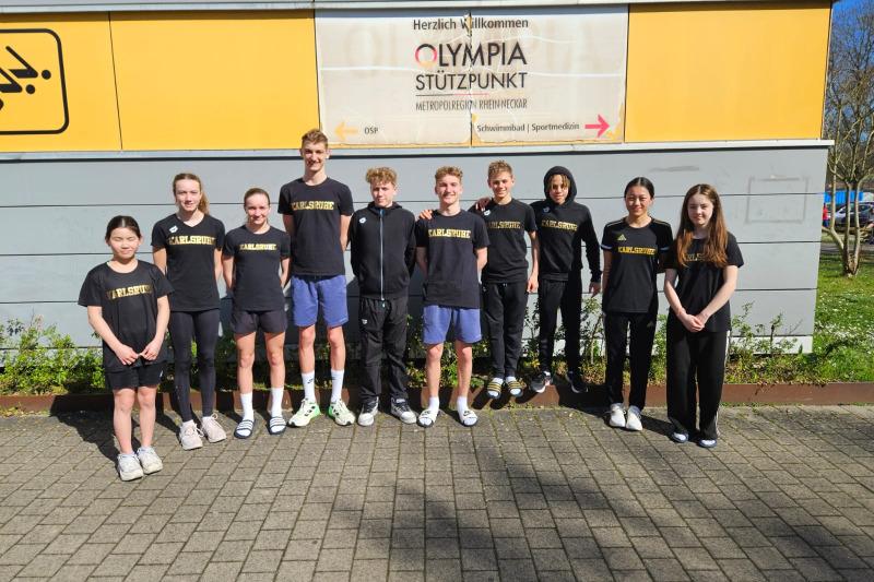 Gruppe von zehn Jugendlichen in schwarzer Sportkleidung vor einem Schild mit der Aufschrift „Olympia Stützpunkt“.