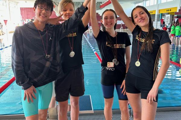 Vier Schwimmer stehen am Schwimmbecken und halten gemeinsam einen Pokal hoch, alle tragen Medaillen.