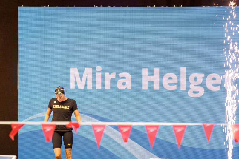 Schwimmerin Mira Helget geht auf die Wettkampfplattform, im Hintergrund ein digitales Display mit ihrem Namen.