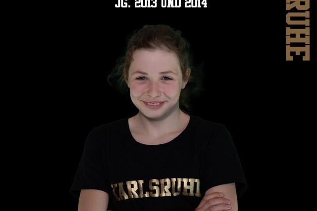 Junge Schwimmerin mit verschränkten Armen, trägt T-Shirt mit „Karlsruhe“, Hintergrund schwarz, Text oben.