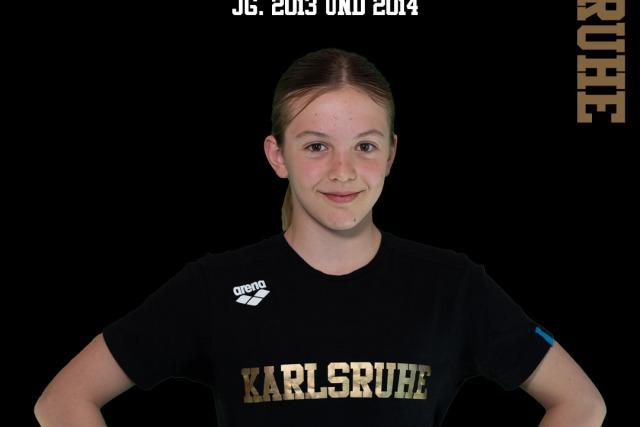 Porträt eines Mädchens in einem schwarzen T-Shirt mit goldener Aufschrift „Karlsruhe“, auf schwarzem Hintergrund.