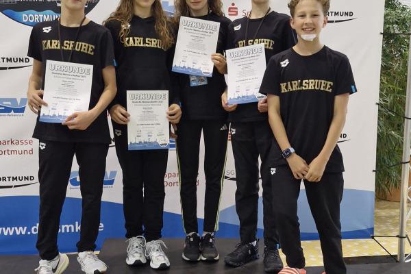 Fünf Kinder in schwarzer Sportkleidung halten Urkunden auf dem Treppchen bei einer Wettkampfveranstaltung in Dortmund.