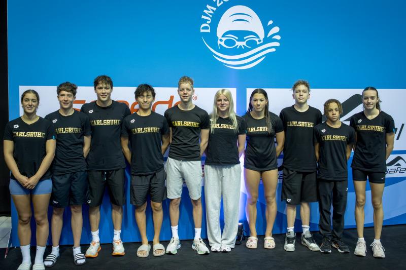 Gruppenfoto von zehn Schwimmern in schwarzen T-Shirts mit der Aufschrift „Karlsruhe“ vor einer blauen Hintergrundwand.