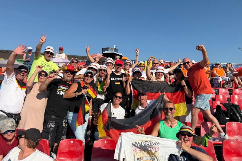 Gruppe von Fans mit deutschen Flaggen und T-Shirts, die in einem Sportstadion jubeln und feiern.