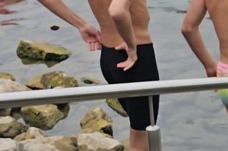 Zwei Schwimmer stehen am Ufer eines Gewässers, einer trägt eine Badekappe und hat Wettkampfnumbers auf den Armen.