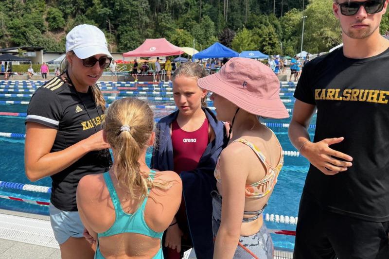 Vier Schwimmerinnen und Schwimmer unterhalten sich am Beckenrand bei einem Wettkampf im Freiwasser.
