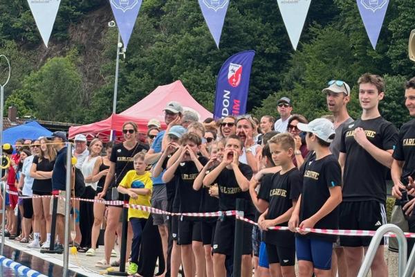 Menschenmenge am Schwimmbeckenrand, Zuschauer unterstützen Schwimmer bei einem Wettkampf in einer belebten Atmosphäre.