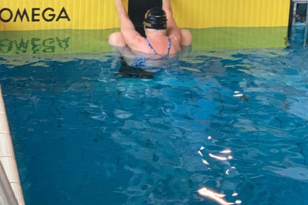 Schwimmerin in einer blauen Badekleidung hängt am Beckenrand eines Schwimmbeckens mit Omega-Startblock.