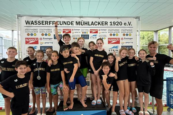 Gruppierung von Schwimmern auf dem Siegertreppchen mit der Aufschrift „Wasserfreunde Mühlacker“ im Hintergrund.