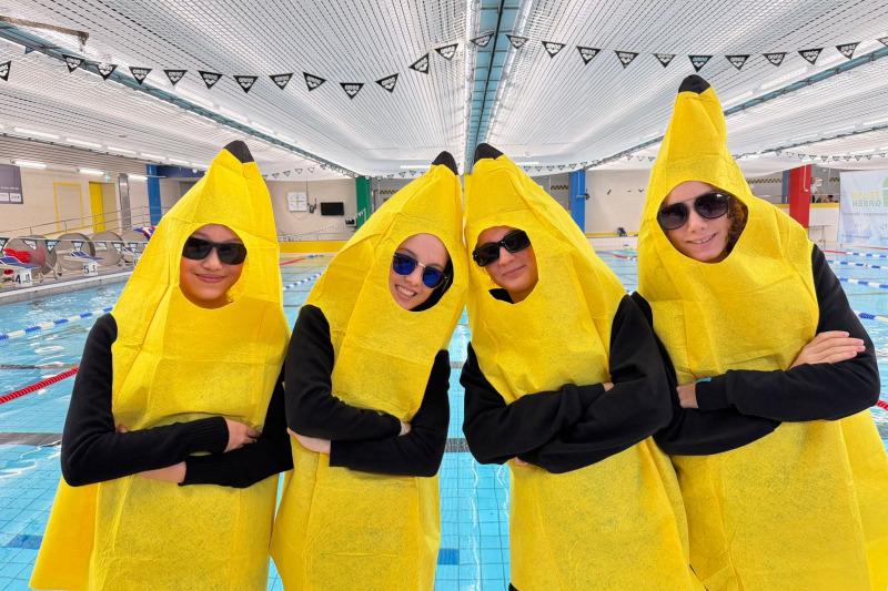 Vier Personen in gelben Bananenkostümen stehen am Rand eines Schwimmbeckens und tragen Sonnenbrillen.