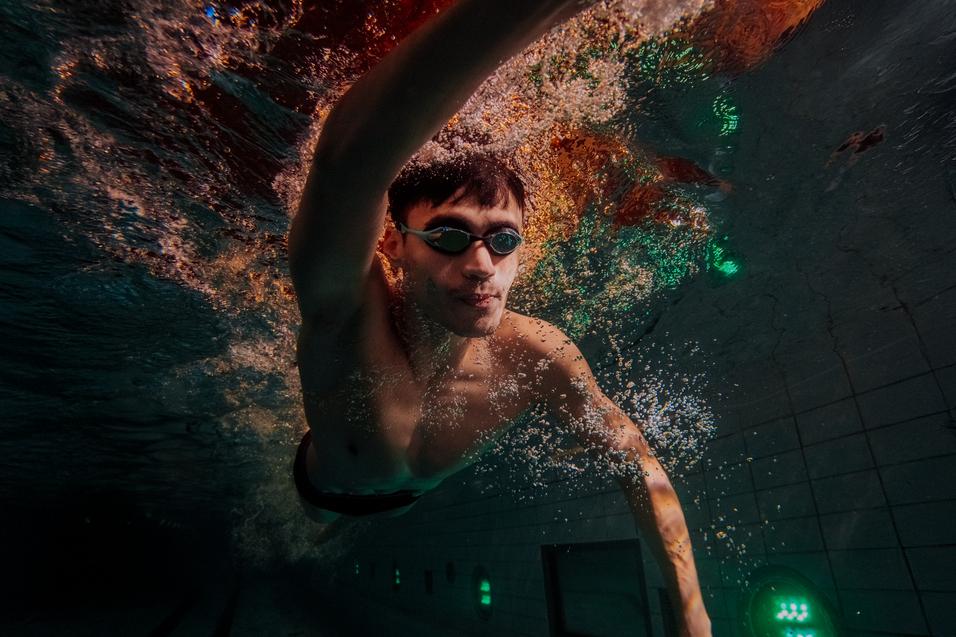 Ein Schwimmer taucht unter Wasser, mit Schwimmbrille und spritzendem Wasser um ihn herum.