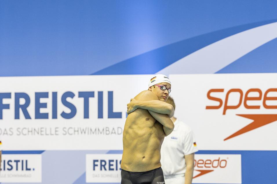 Schwimmer in Sportkleidung, bereitet sich auf den Wettkampf an einer Schwimmbeckenrand vor, Hintergr&uuml;nde mit Sponsorenlogos.
