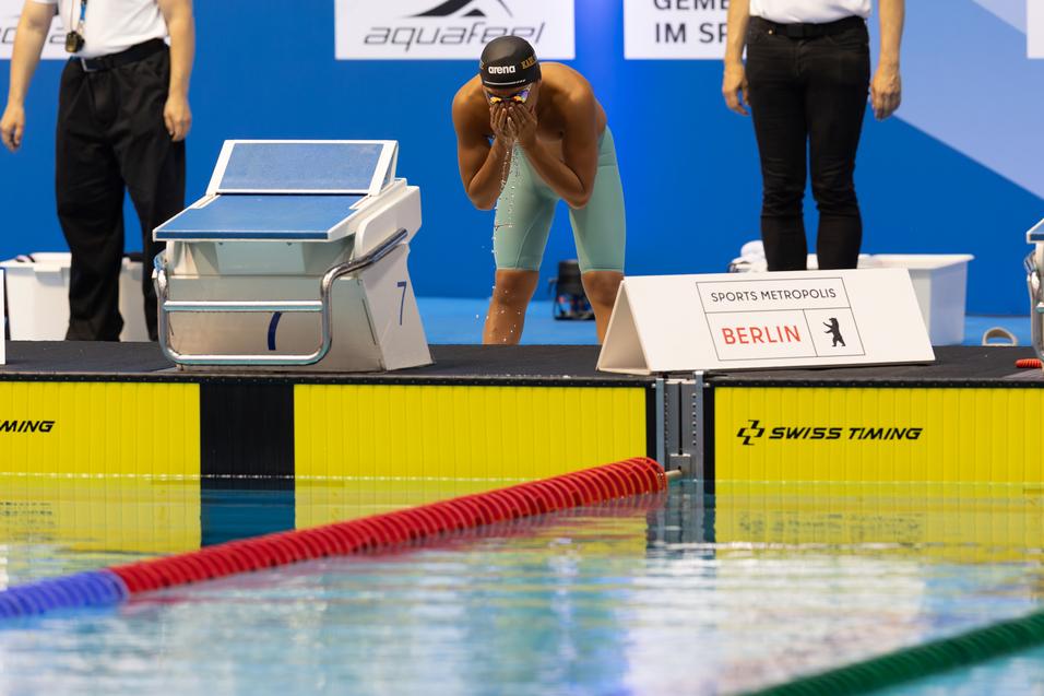 Schwimmer bereitet sich an der Startblockkante auf den Wettkampf vor, w&auml;hrend das Wasserspiegelbild reflektiert.