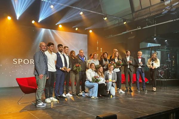Gruppe von Sportlern mit Blumen beim Event auf einer B&uuml;hne, beleuchtet von farbigen Scheinwerfern im Hintergrund.