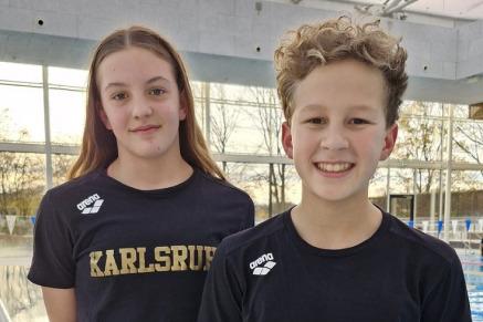 Zwei Kinder in schwarzen T-Shirts mit dem Aufdruck "Karlsruhe" stehen vor einem Schwimmbecken.