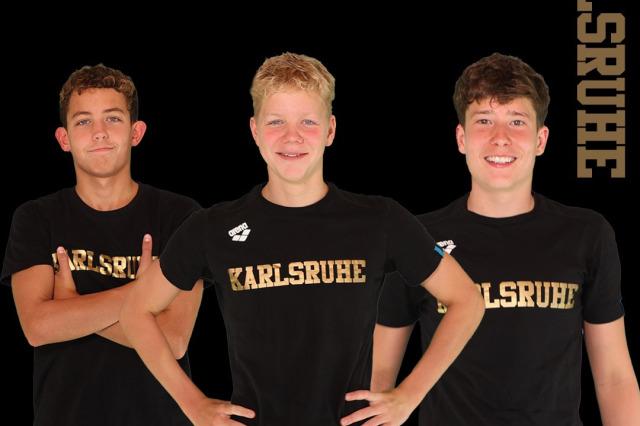 Drei junge Sportler in schwarzen T-Shirts mit "Karlsruhe" posieren f&uuml;r ein Gruppenbild. Hintergrund: Stadtansicht Rostock.