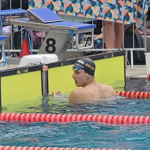 Schwimmer in der Badehose mit Kappe schaut &uuml;ber den Beckenrand, Schwimmhalle mit gepunkteten Schwimmbahnen im Hintergrund.