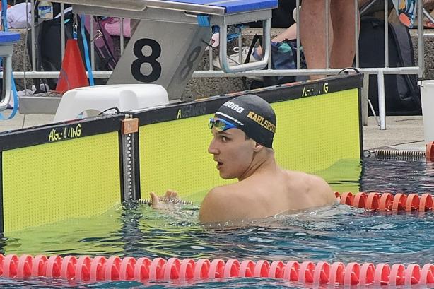 Schwimmer in der Badehose mit Kappe schaut &uuml;ber den Beckenrand, Schwimmhalle mit gepunkteten Schwimmbahnen im Hintergrund.