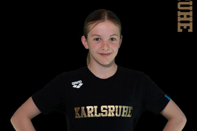 Portr&auml;t eines M&auml;dchens in einem schwarzen T-Shirt mit goldener Aufschrift &bdquo;Karlsruhe&ldquo;, auf schwarzem Hintergrund.