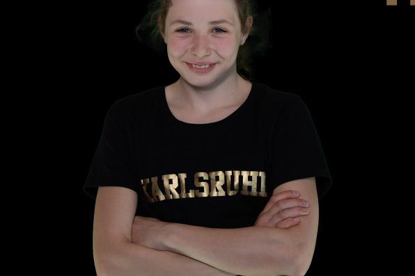 Junge Schwimmerin mit verschr&auml;nkten Armen, tr&auml;gt T-Shirt mit &bdquo;Karlsruhe&ldquo;, Hintergrund schwarz, Text oben.