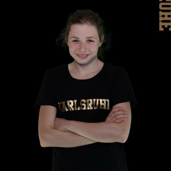 Junge Schwimmerin mit verschr&auml;nkten Armen, tr&auml;gt T-Shirt mit &bdquo;Karlsruhe&ldquo;, Hintergrund schwarz, Text oben.