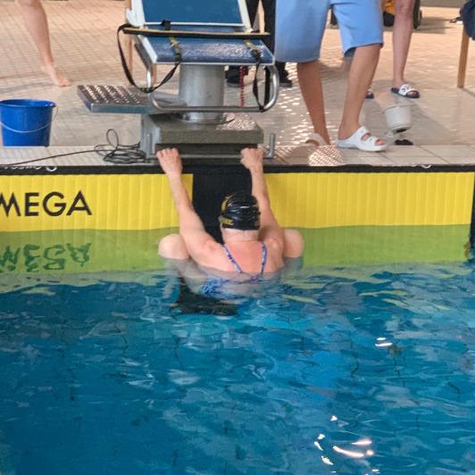 Schwimmerin in einer blauen Badekleidung hängt am Beckenrand eines Schwimmbeckens mit Omega-Startblock.
