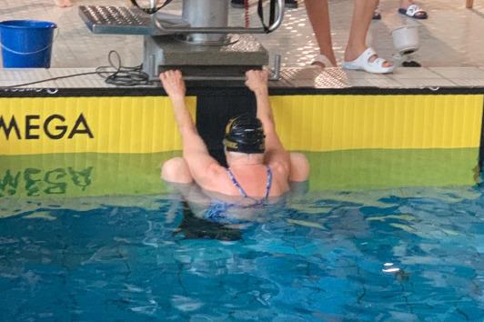 Schwimmerin in einer blauen Badekleidung hängt am Beckenrand eines Schwimmbeckens mit Omega-Startblock.