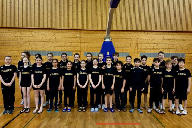Gruppenshot von Kindern in schwarzen T-Shirts mit &bdquo;Karlsruhe&ldquo;, auf einem Basketballfeld in einer Sporthalle.