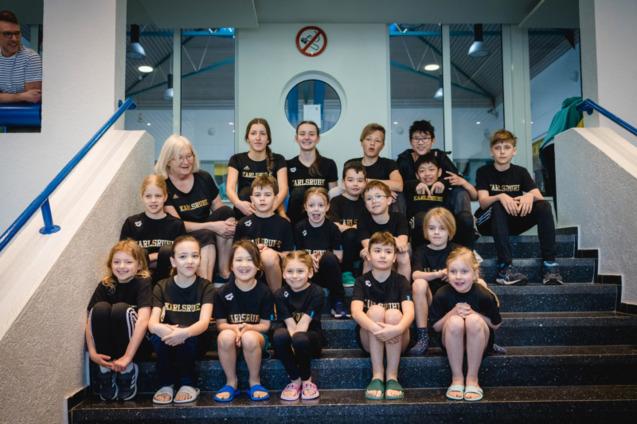 Gruppenfoto von Kindern und Jugendlichen in schwarzen T-Shirts mit der Aufschrift &bdquo;Karlsruhe&ldquo;, sitzend auf Treppenstufen.