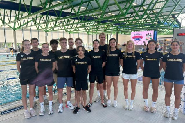 Gruppe von Schwimmern in schwarzen T-Shirts mit der Aufschrift &bdquo;Karlsruhe&ldquo; in einer Schwimmhalle.