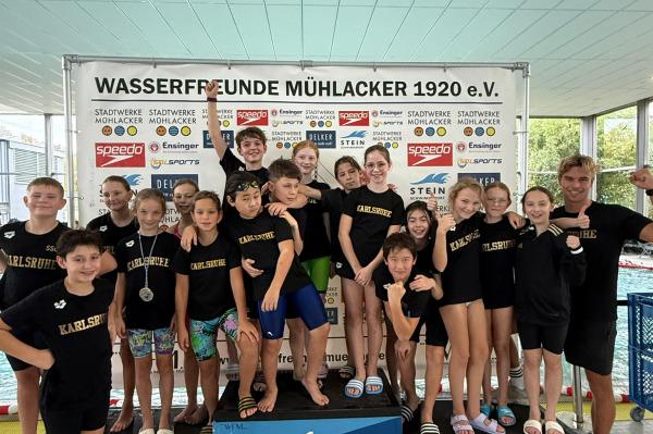 Gruppierung von Schwimmern auf dem Siegertreppchen mit der Aufschrift &bdquo;Wasserfreunde M&uuml;hlacker&ldquo; im Hintergrund.
