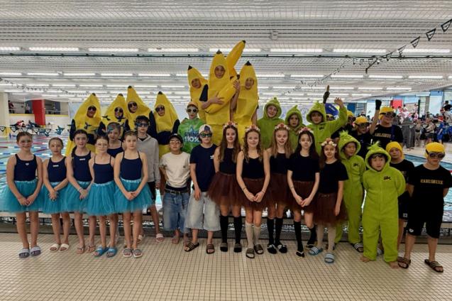 Gruppennfoto von Kindern in lustigen Kost&uuml;men, darunter Bananen und Ungeheuer, vor einem Schwimmbecken.
