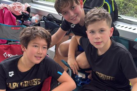 Drei Jungen in Sportkleidung sitzen lächelnd auf Campingstühlen in einer Sporteinrichtung.